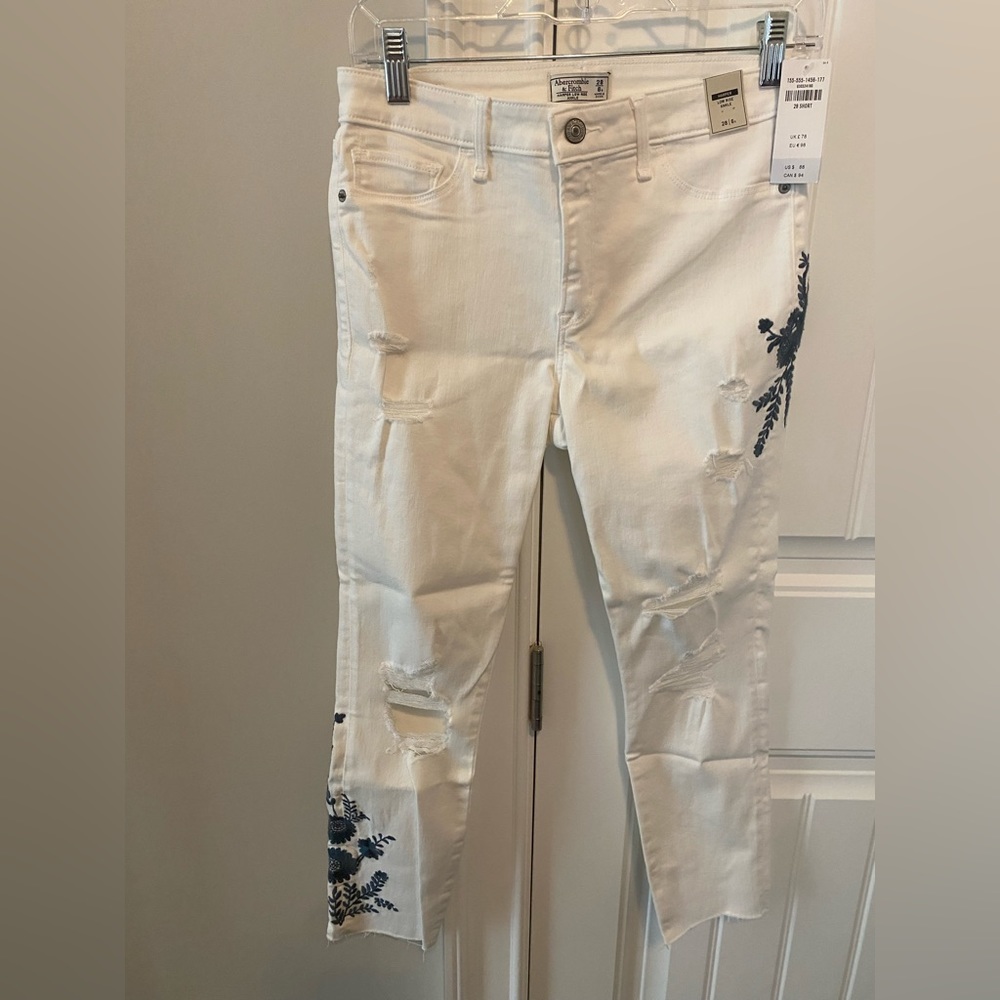 White cropped jeans, 6 short. Blue flowered embroidery on R thigh, L shin.